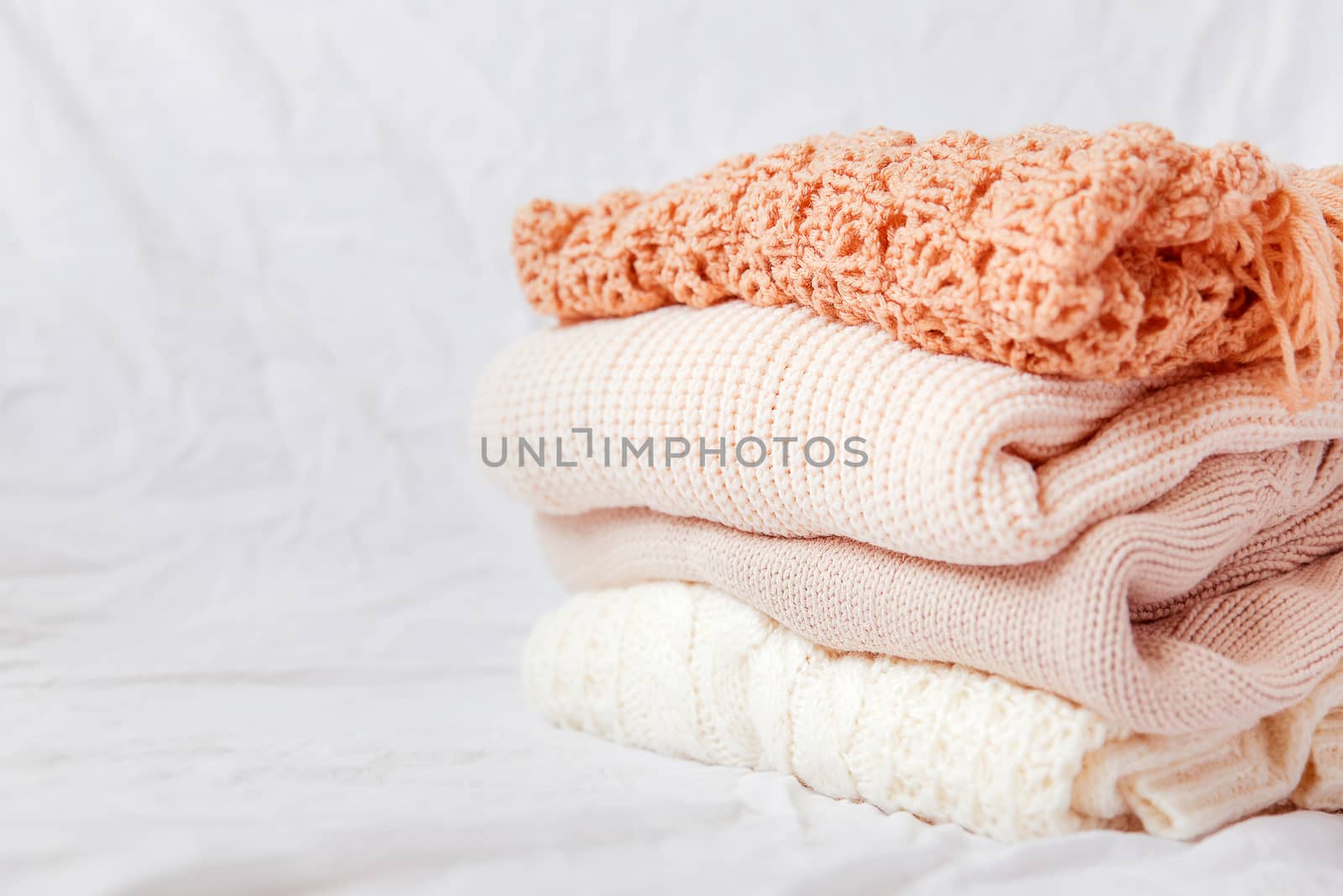 Pile of beige woolen clothes on a white background. Warm knitted sweaters and scarfs are folded in one heap.