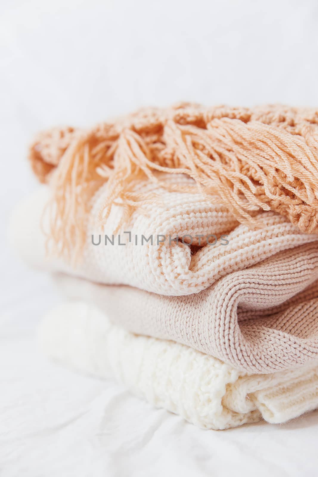 Pile of beige woolen clothes on a white background. Warm knitted sweaters and scarfs are folded in one heap.