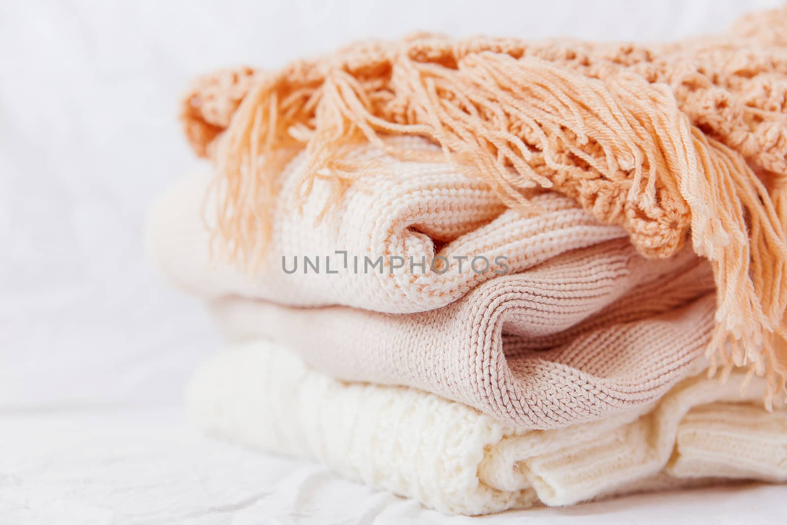 Pile of beige woolen clothes on a white background. Warm knitted sweaters and scarfs are folded in one heap.