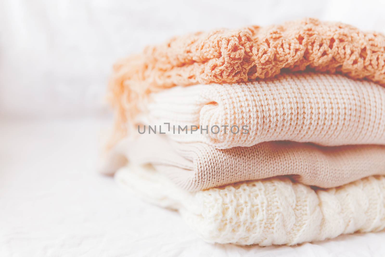 Pile of beige woolen clothes on a white background. Warm knitted sweaters and scarfs are folded in one heap. Imitation of Instagram style tone.