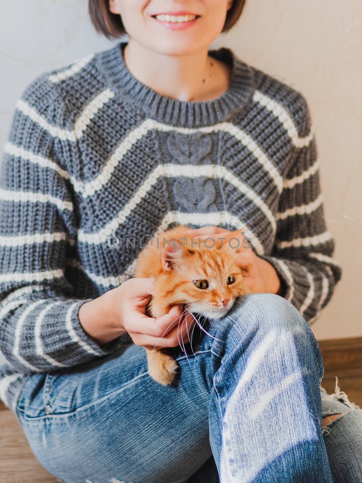 Cute ginger cat dozing on woman knees. Smiling woman in torn jeans stroking her fluffy pet. Cozy home.