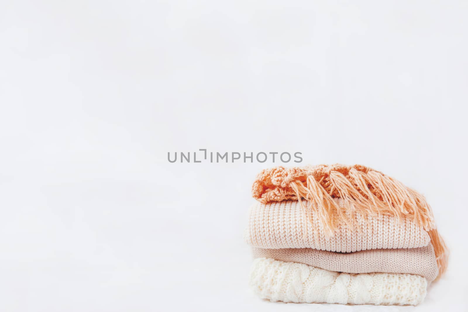 Pile of beige woolen clothes on a white background. Warm knitted sweaters and scarfs are folded in one heap. Place for text.