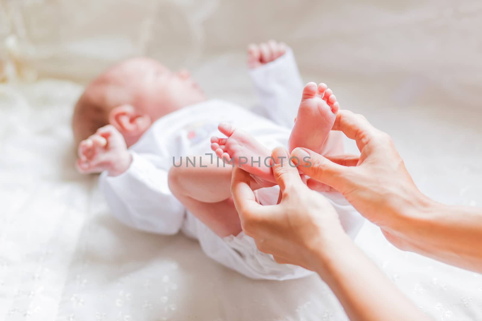 Mother holds newborn baby's bare heels. Tiny feet in woman's hand. Cozy morning at home.