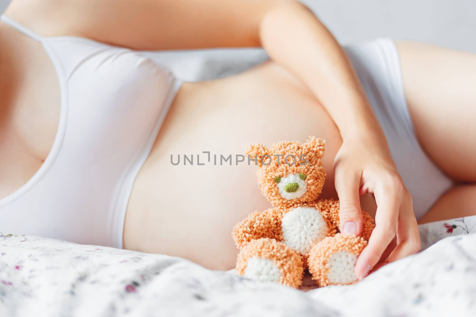 Pregnant woman in white underwear with toy bear. Young woman expecting a baby.