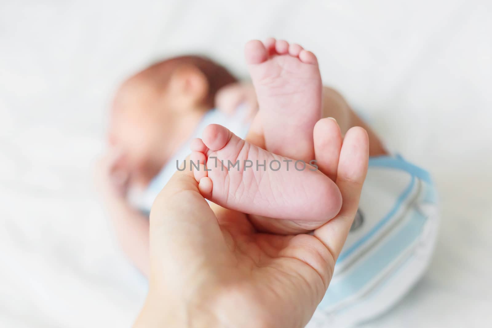 Mother holds newborn baby's bare heels. Tiny feet in woman's hand. Cozy morning at home.