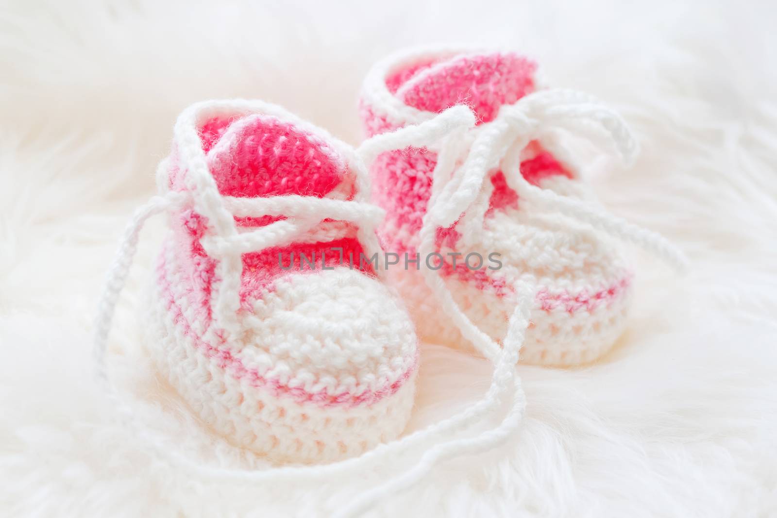 Little baby shoes. Hand knitted first sneakers for newborn girl. Crochet handmade pink bootees on fluffy white background.