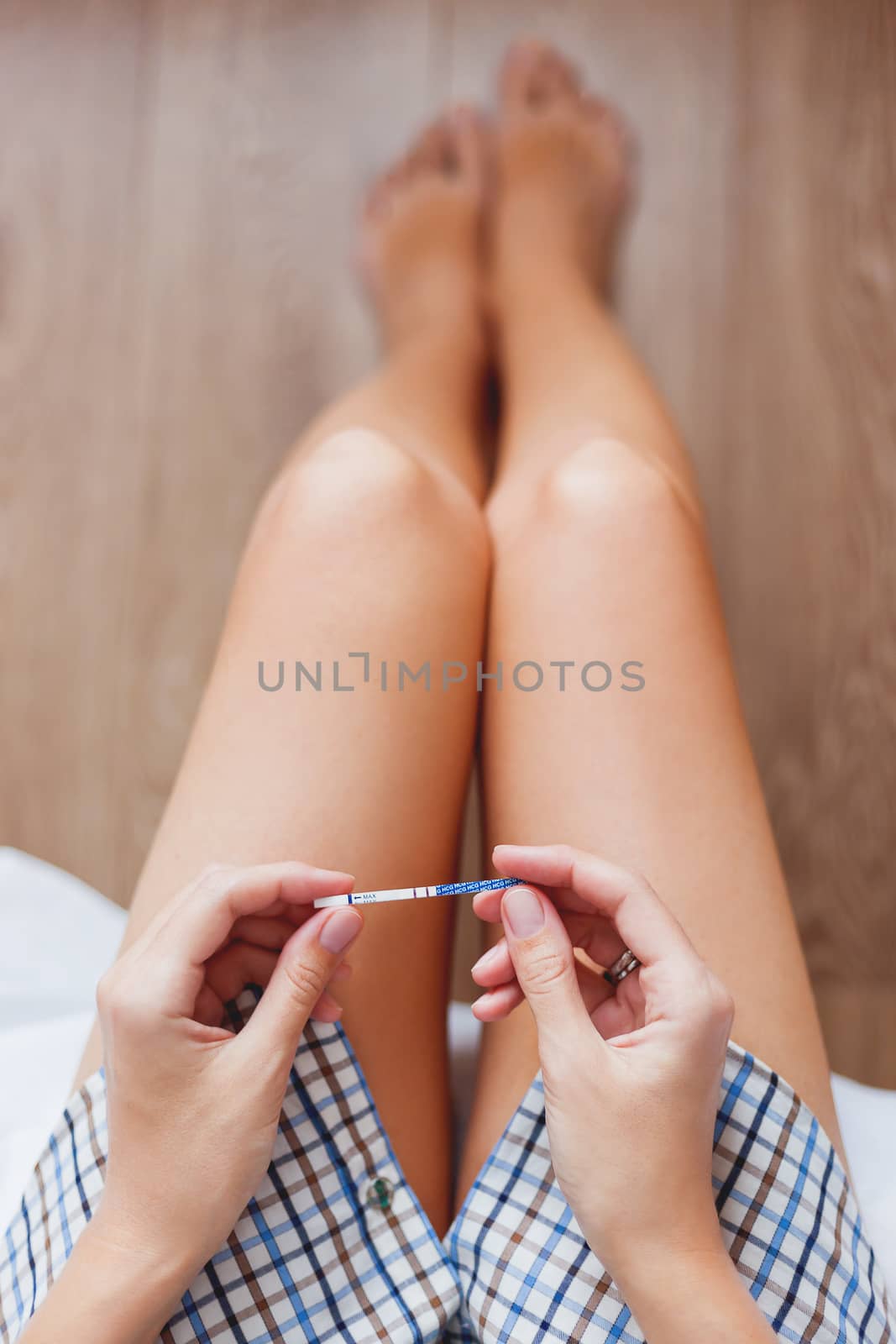 Woman in shirt sitting on bed with positive pregnancy test in hands. Woman is expecting baby. Cozy happy morning at home.