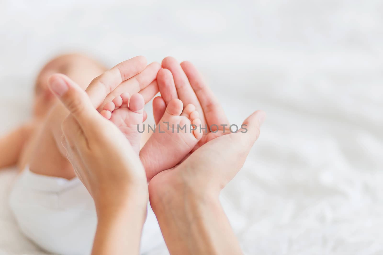 Mother holds newborn baby's bare feet. Tiny feet in woman's hand. Cozy morning at home.