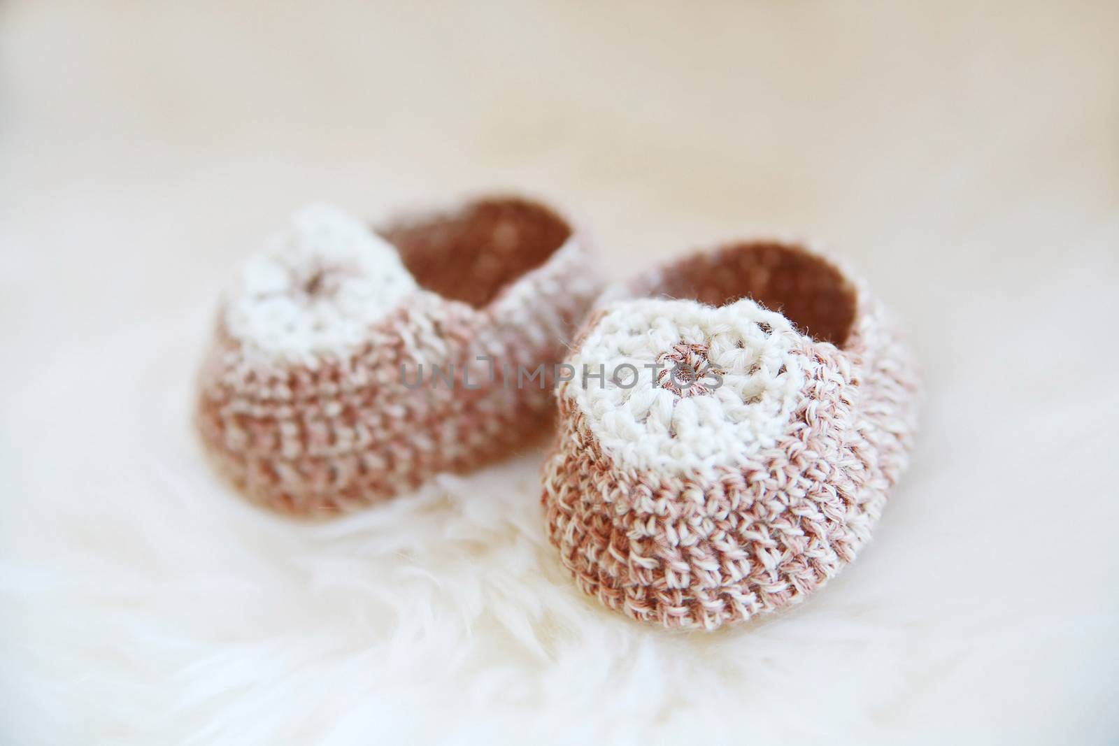 Little baby shoes. Hand knitted first bootees for newborn girl. Crochet handmade beige bootees on fluffy white background.
