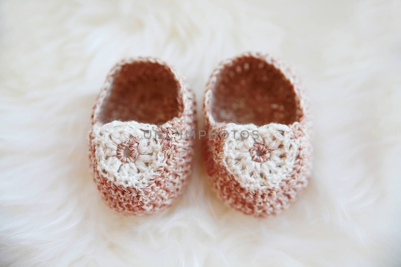 Little baby shoes. Hand knitted first bootees for newborn girl. Crochet handmade beige bootees on fluffy white background.