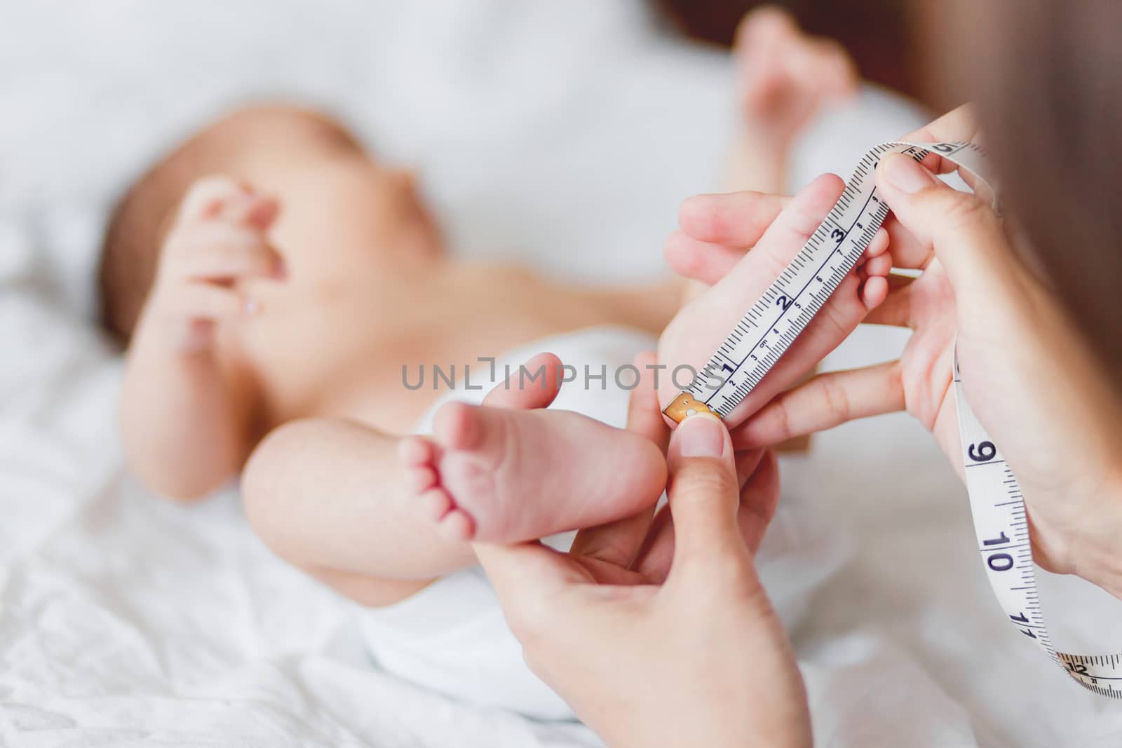 Mother holds newborn baby's bare feet and measures the length of foot. Cozy morning at home.