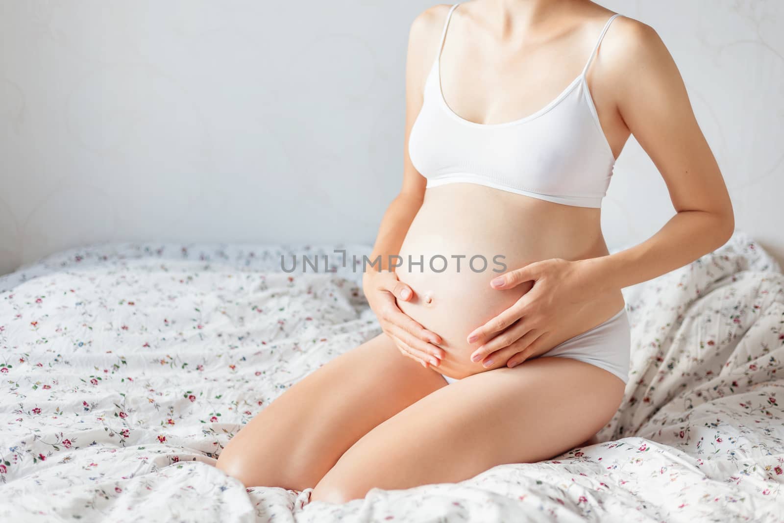 Pregnant woman in white underwear on bed. Young woman expecting a baby.