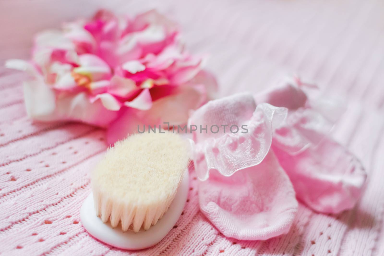 First accessories for newborn girl - pink booties, hat with silk flower and tiny hair brush. Cute pink background.