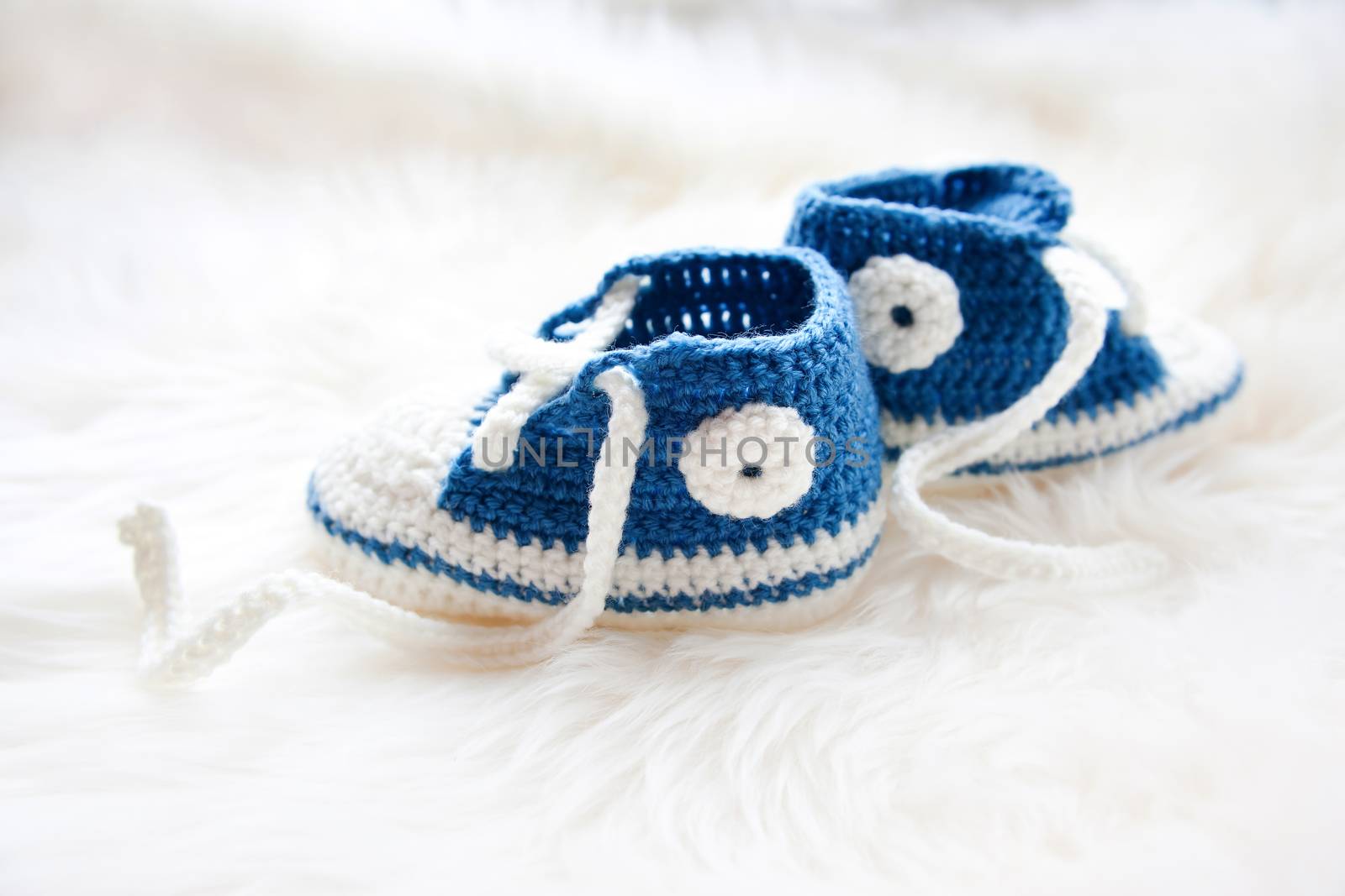 Little baby shoes. Handknitted first sneakers for newborn boy or girl. Crochet handmade bootees on fluffy white background.