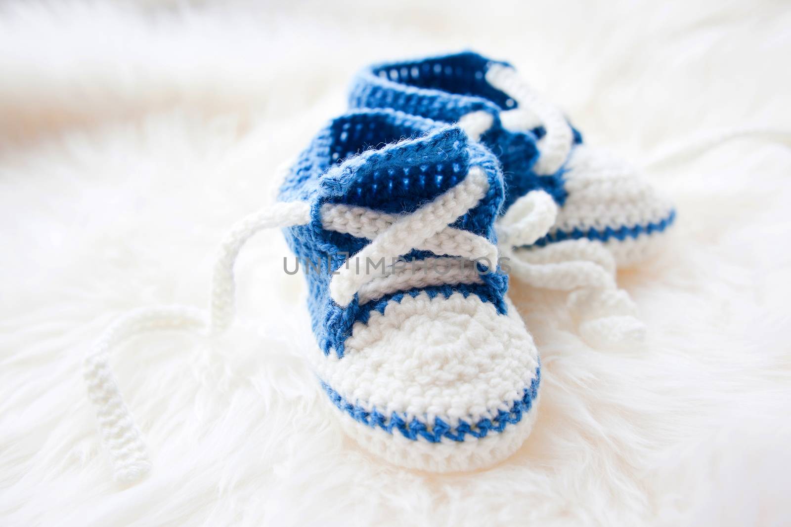 Little baby shoes. Handknitted first sneakers for newborn boy or girl. Crochet handmade bootees on fluffy white background.