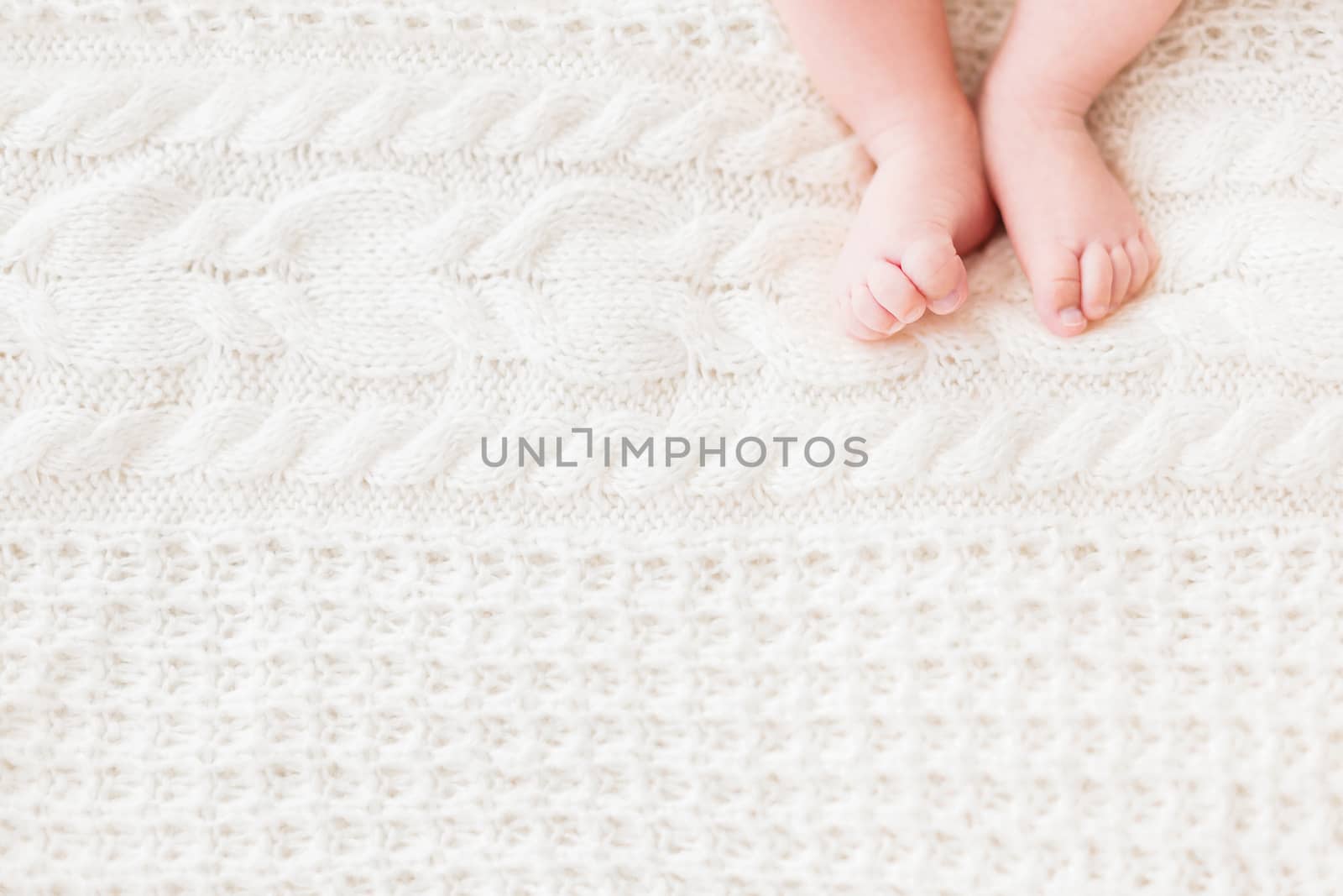 Baby's feet on white knitted background. Little child's bare feet. Cozy morning bedtime at home. Place for text.