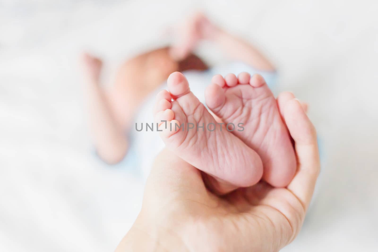 Mother holds newborn baby's bare heels. Tiny feet in woman's hand. Cozy morning at home.
