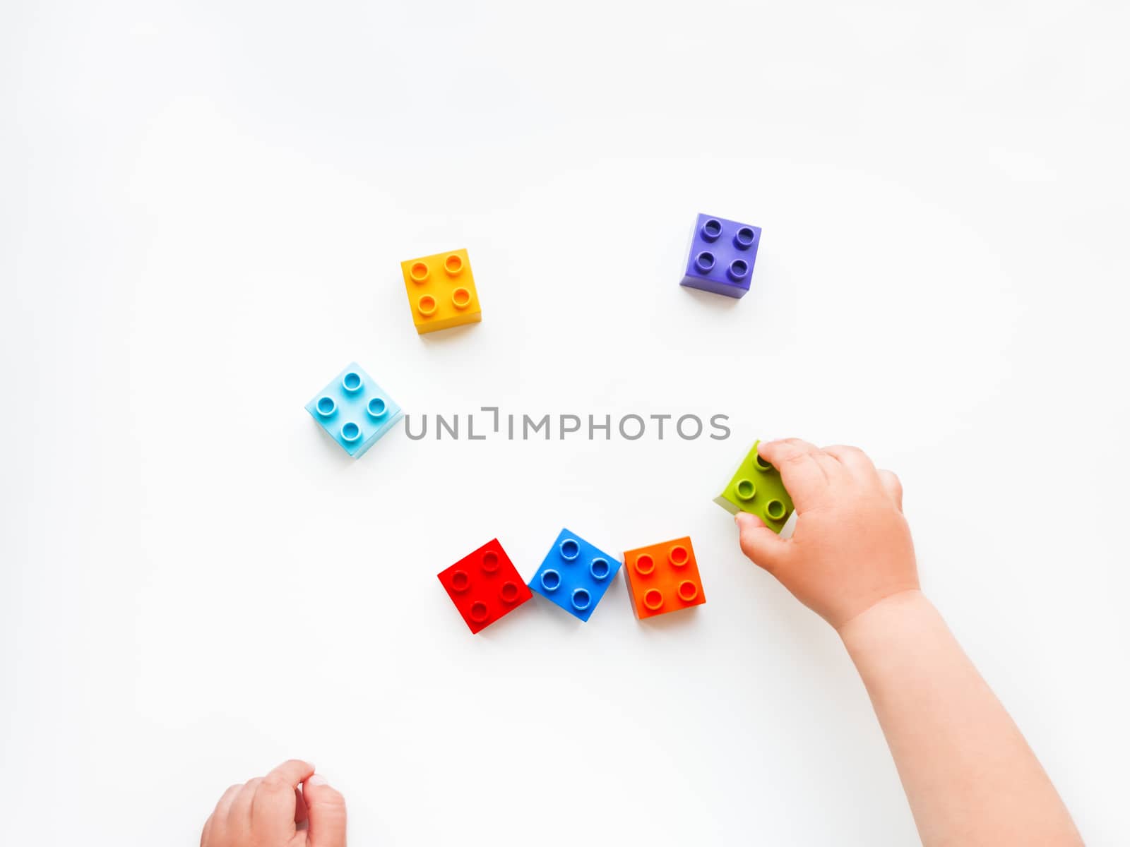 Child is playing with colorful constructor blocks. Kid's hands with bricks toy on white background. Educational toy, flat lay, top view.