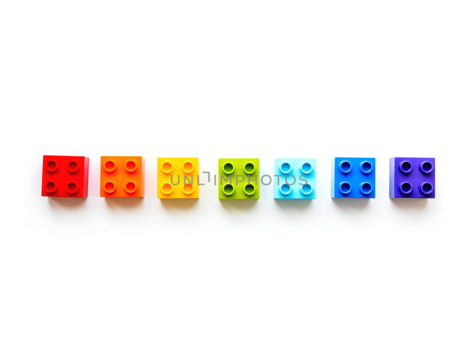 Set of colorful constructor blocks. Seven rainbow colored toy bricks lying in order. Education process - learning colors and numbers with child using multicolored toy details.