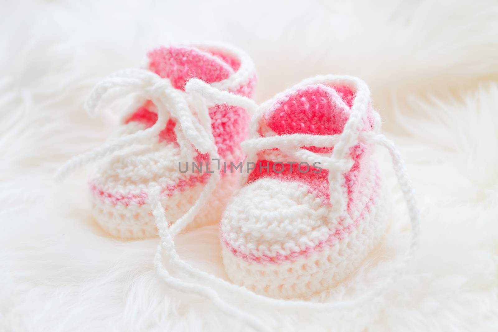 Little baby shoes. Hand knitted first sneakers for newborn girl. Crochet handmade pink bootees on fluffy white background.