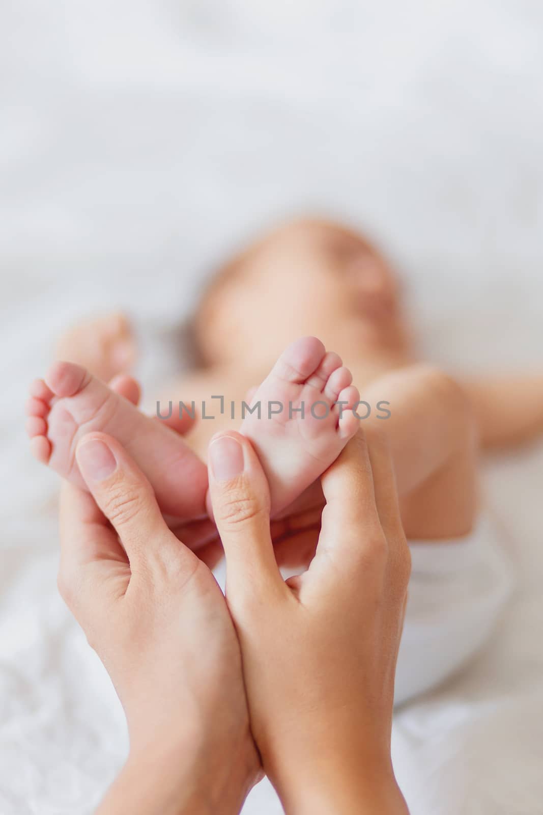 Mother holds newborn baby's bare feet. Tiny feet in woman's hand. Cozy morning at home.