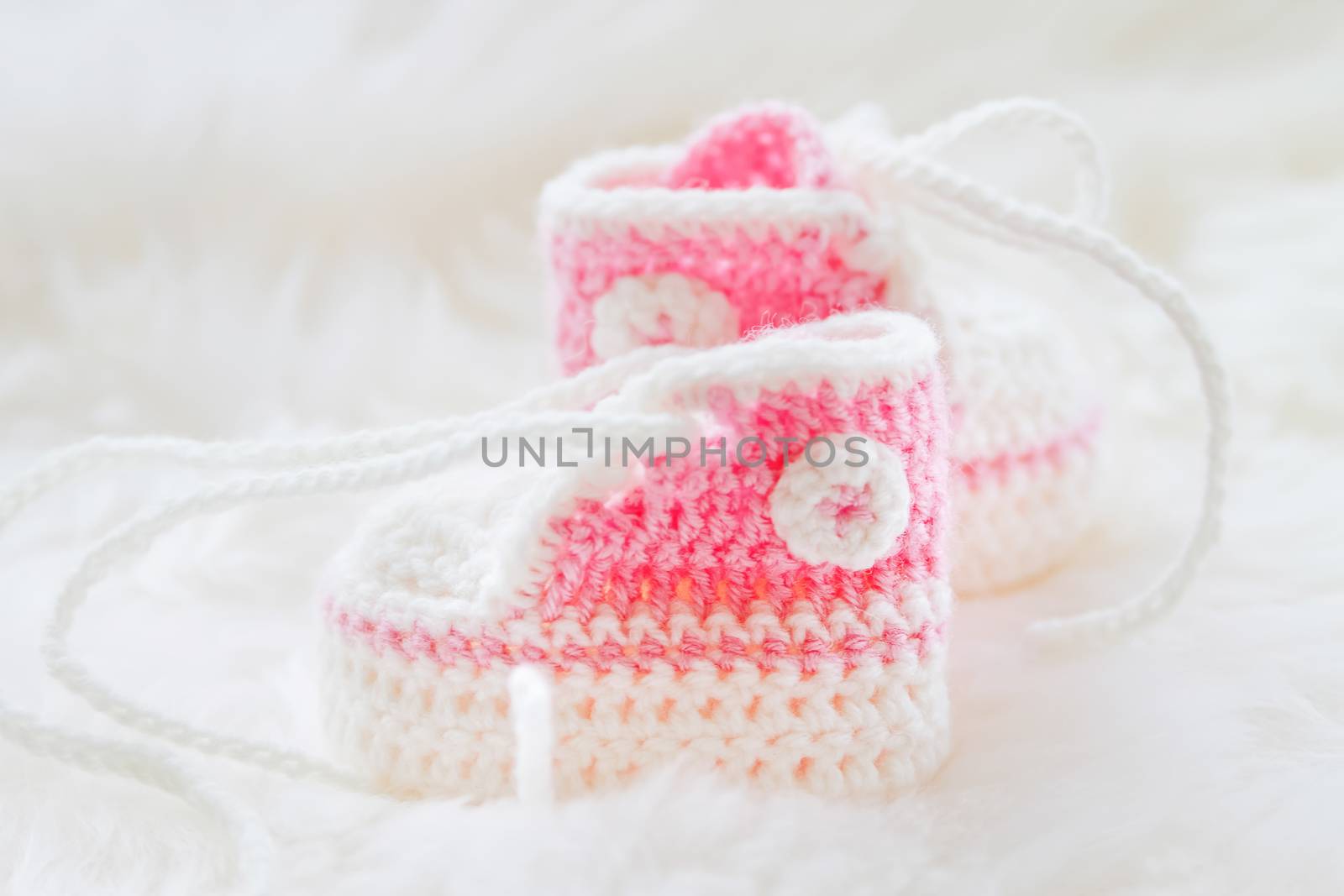 Little baby shoes. Hand knitted first sneakers for newborn girl. Crochet handmade pink bootees on fluffy white background.