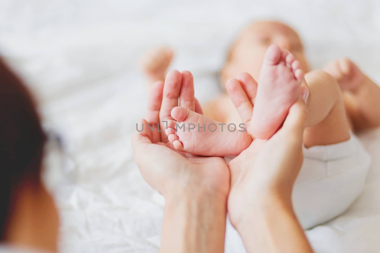 Mother holds newborn baby's bare feet. Tiny feet in woman's hand. Cozy morning at home.