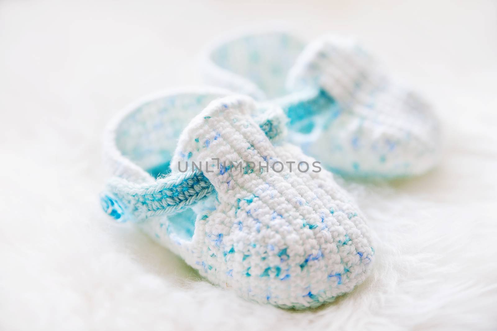 Little baby shoes. Handknitted first shoes for boy or girl. Crochet handmade bootees on white fluffy background.