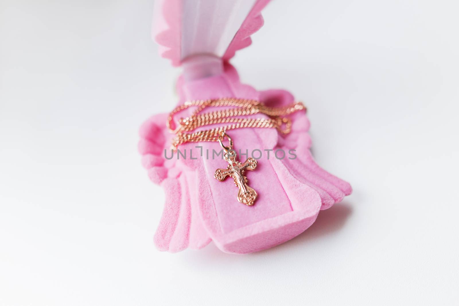 Golden cross for christening on pink gift box in shape of praying angel. Elegant religious accessory for little baby girl. Russian Orthodox church ceremony details.