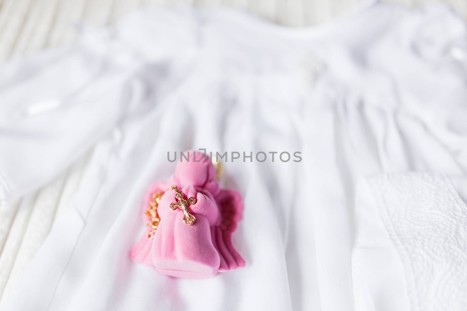 Golden cross for christening on pink gift box in shape of praying angel. Laced dress for christening. Russian Orthodox church ceremony details.Elegant religious accessory for little baby girl. Russian Orthodox church ceremony details.
