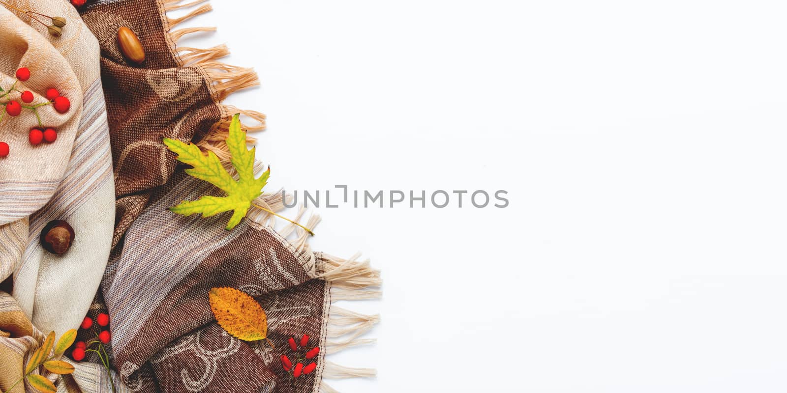 Beige scarf with fallen leaves and berries on white background. Folded warm accessory with copy space.