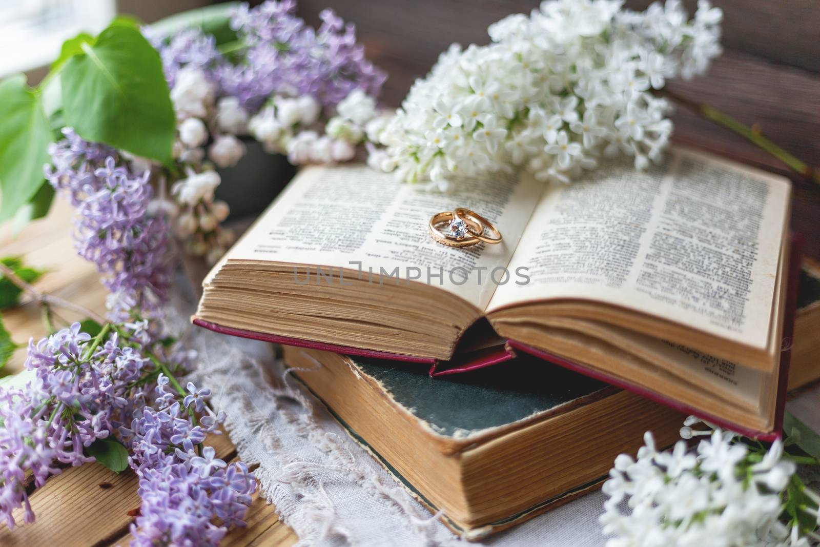 Pair of wedding rings with diamond. Rustic background with old books and lilac flowers. Retro background.