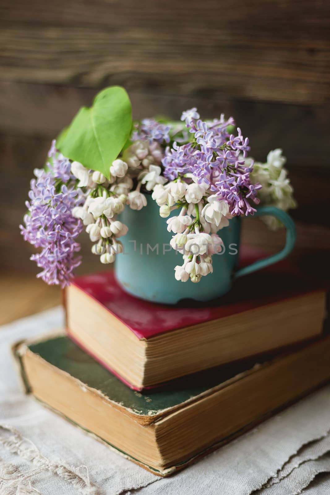 Two old books and rusty mug with lilac bouquet on homespun napkin. Interesting reading, vintage background.
