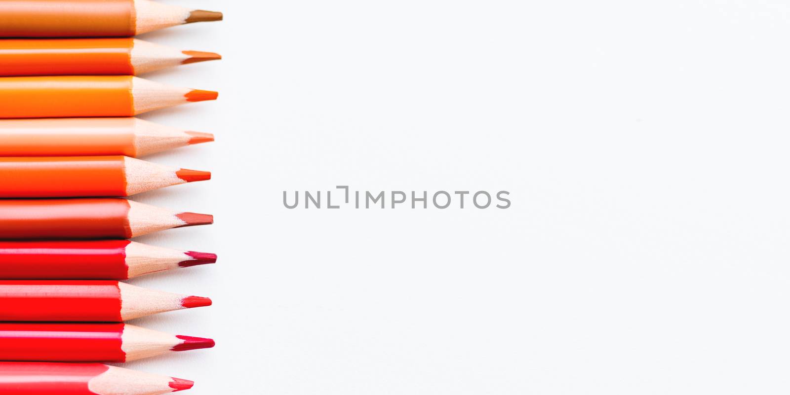 Row of colorful red and orange pencils on white background. School supplies on blackboard. Kid's stationery. Back to school copy space backdrop.