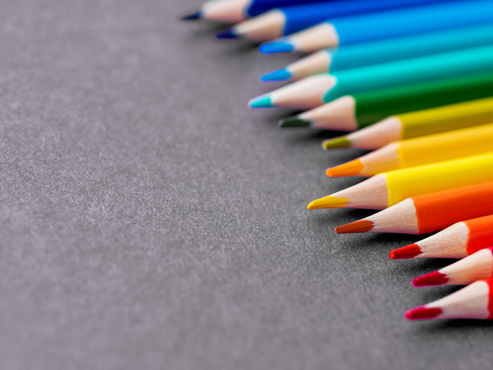 Row of colorful watercolor pencils on dark grey background. School supplies on purple black background. Kid's stationery. Back to school textured backdrop.
