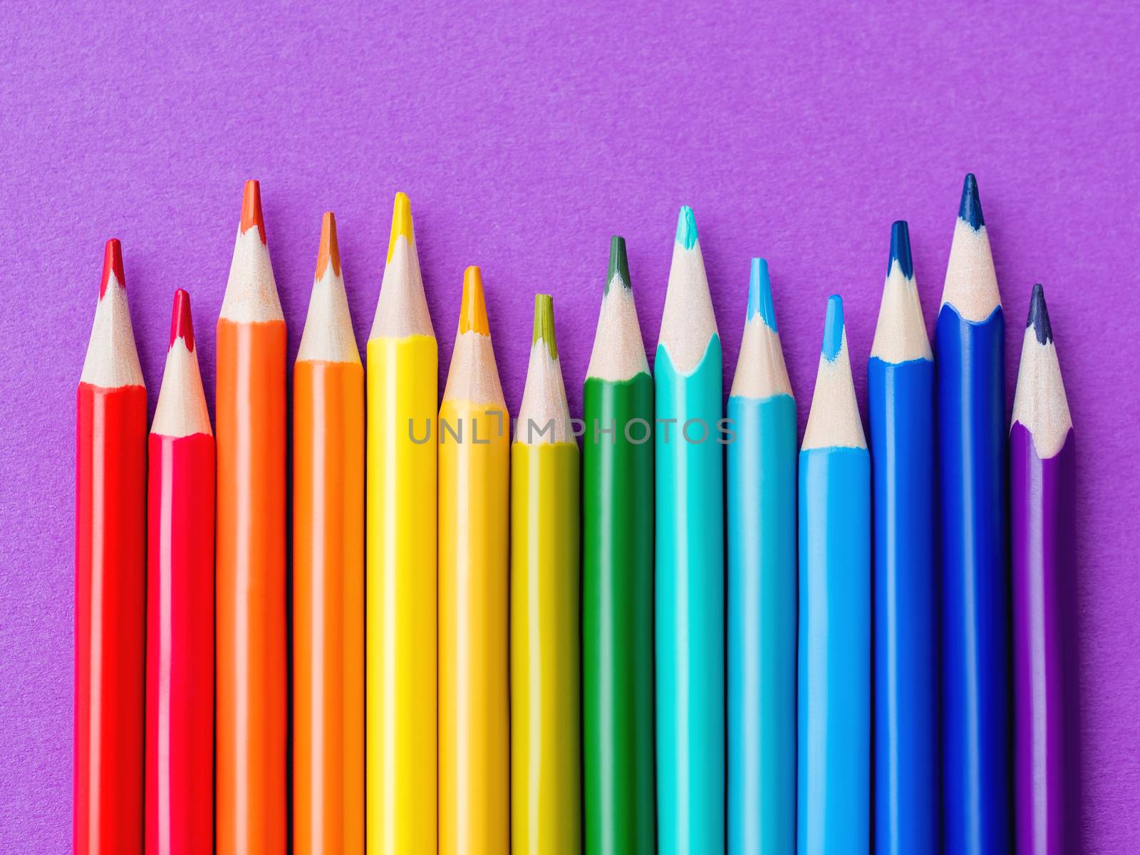 Row of colorful watercolor pencils on lilac background. School supplies on purple paper background. Kid's stationery. Back to school magenta backdrop.