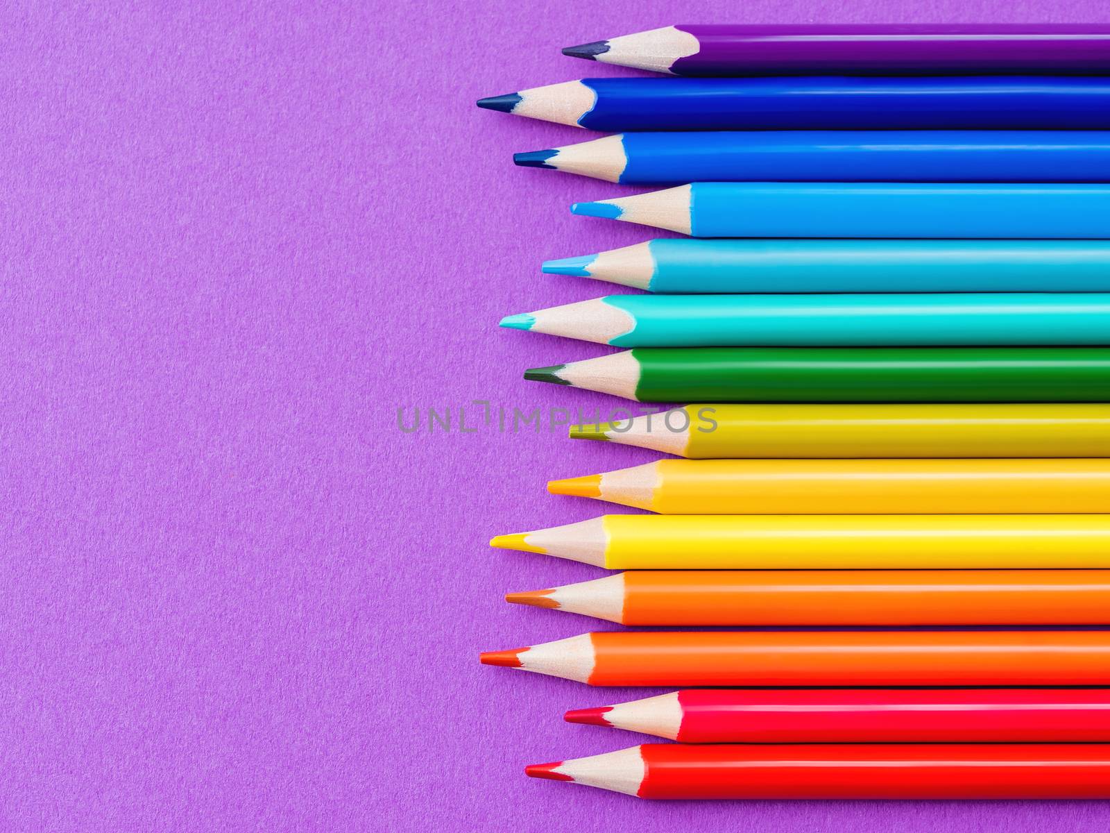 Horizontal row of colorful pencils on purple paper background. School supplies in colores of rainbow. Kid's stationery with magenta copy space. Back to school lilac backdrop.