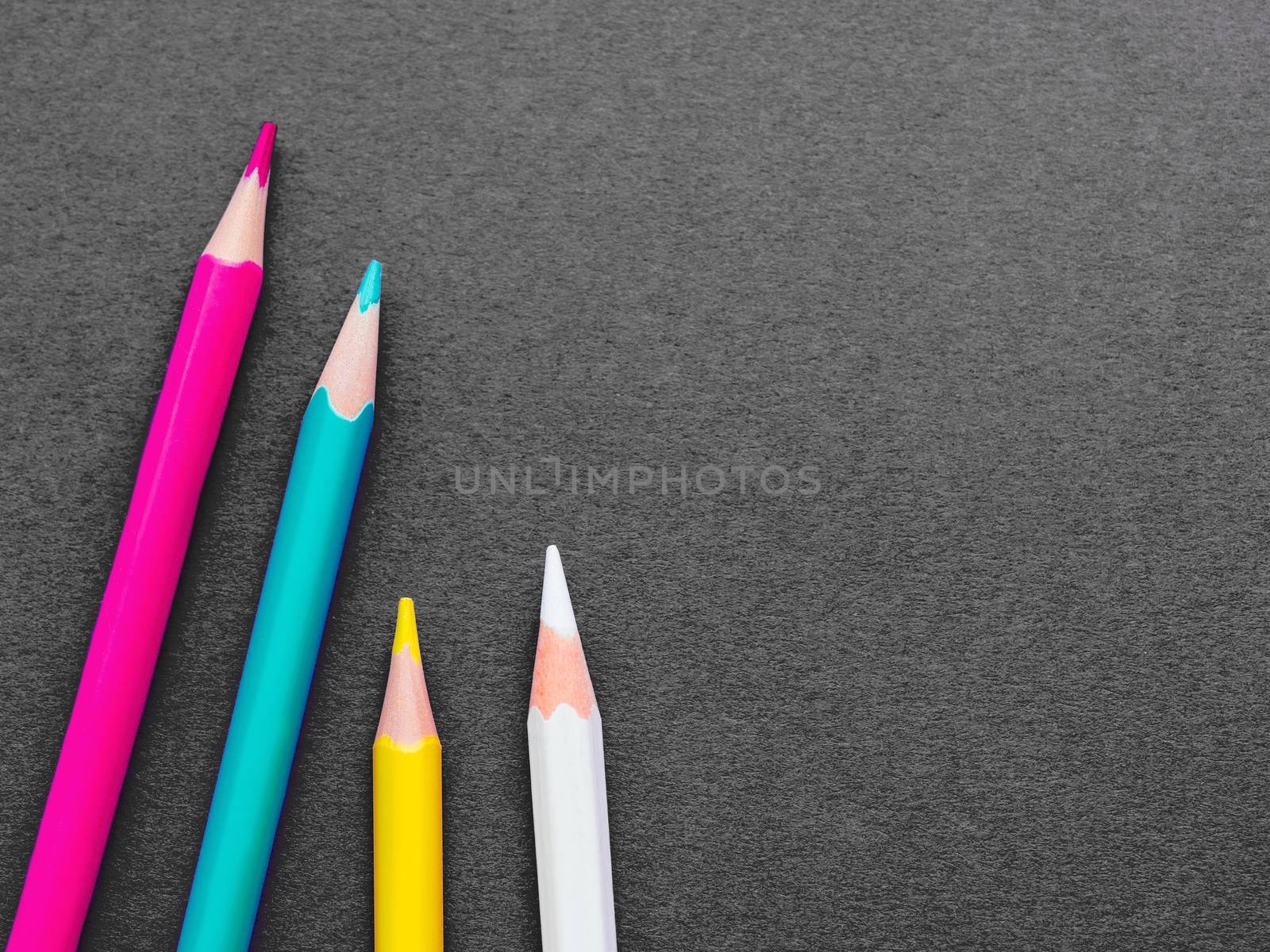 Row of colorful watercolor pencils on dark grey paper background. School supplies on blackboard. Kid's stationery. Back to school black backdrop.