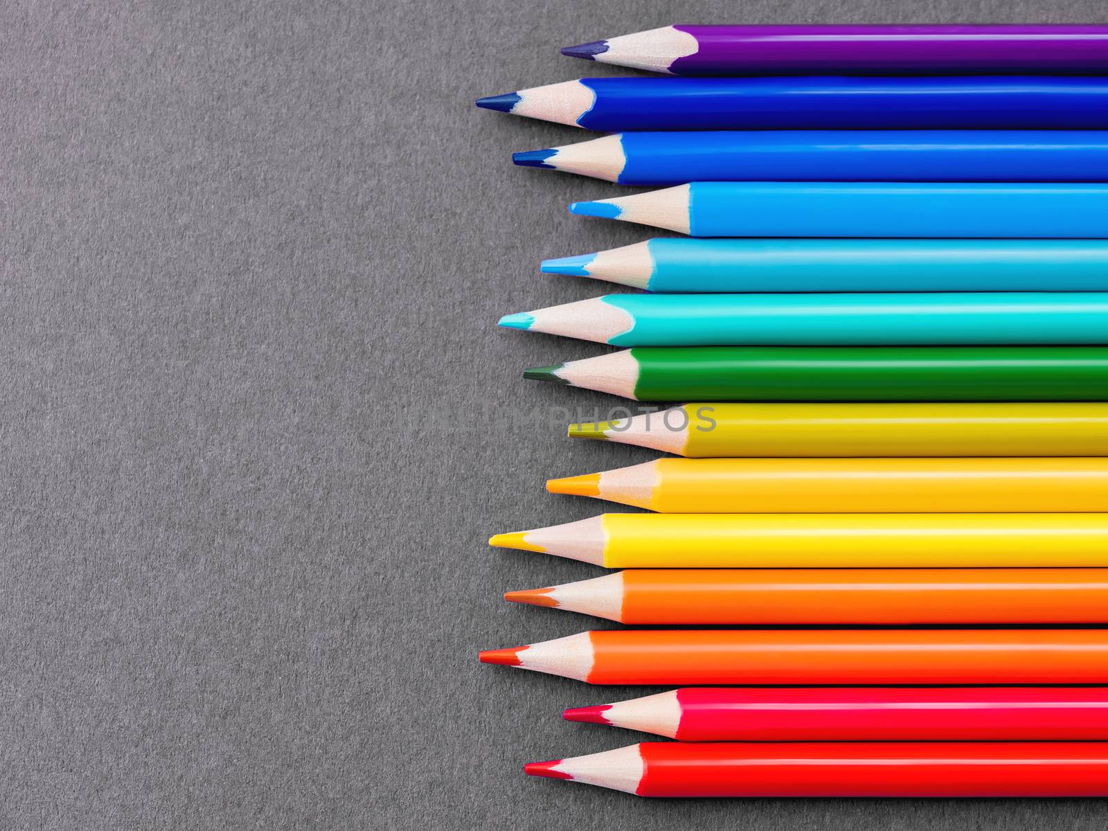 Horizontal row of colorful pencils on grey paper background. School supplies in colores of rainbow on blackboard. Kid's stationery with black copy space. Back to school backdrop.
