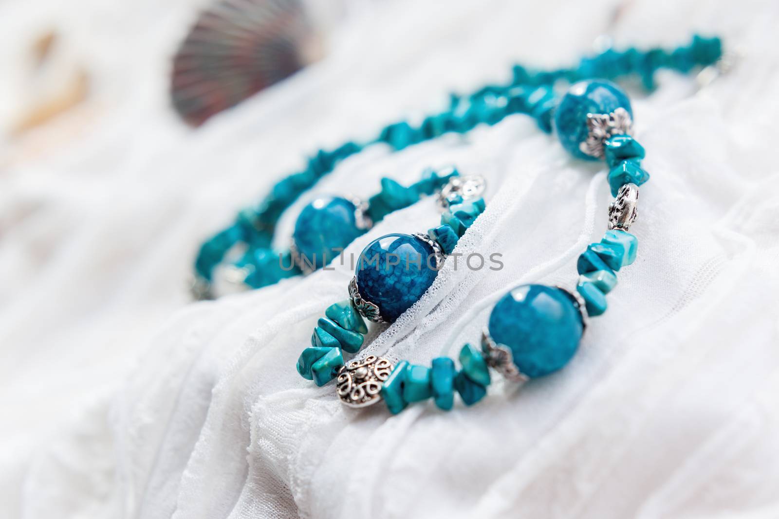 Women jewelry with blue natural stones. Agate beads on white fabric with ruches.