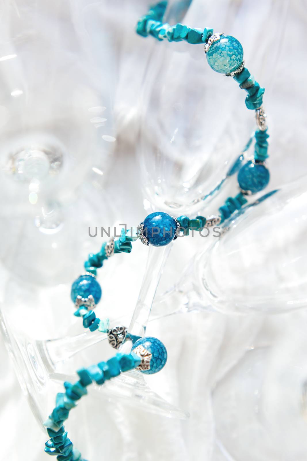 Women jewelry with blue natural stones. Agate beads on clear transparent wineglasses.