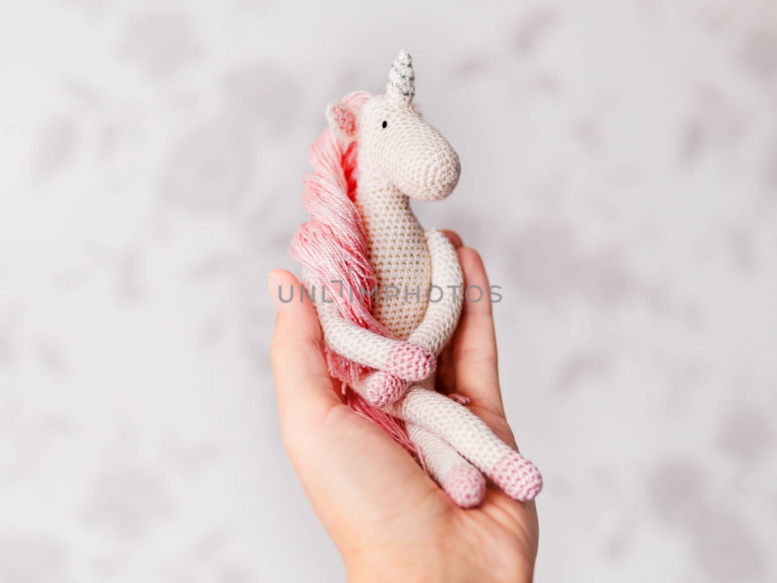 Cute fairy unicorn with a pink mane and a tail made of threads. Crocheted hand made toy on woman palm. Trendy creature, symbol of magic and miracles.