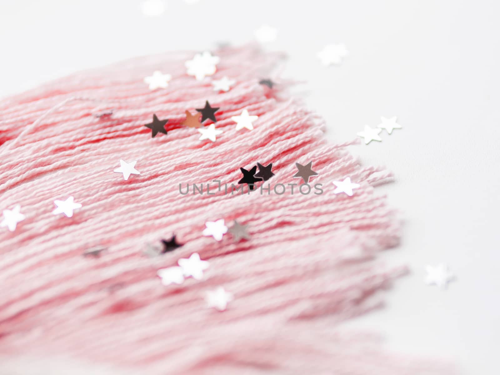 Pink mane and tail of cute unicorn made of threads. Crocheted hand made toy on white background with silver stars confetti. Trendy creature, symbol of magic and miracles.
