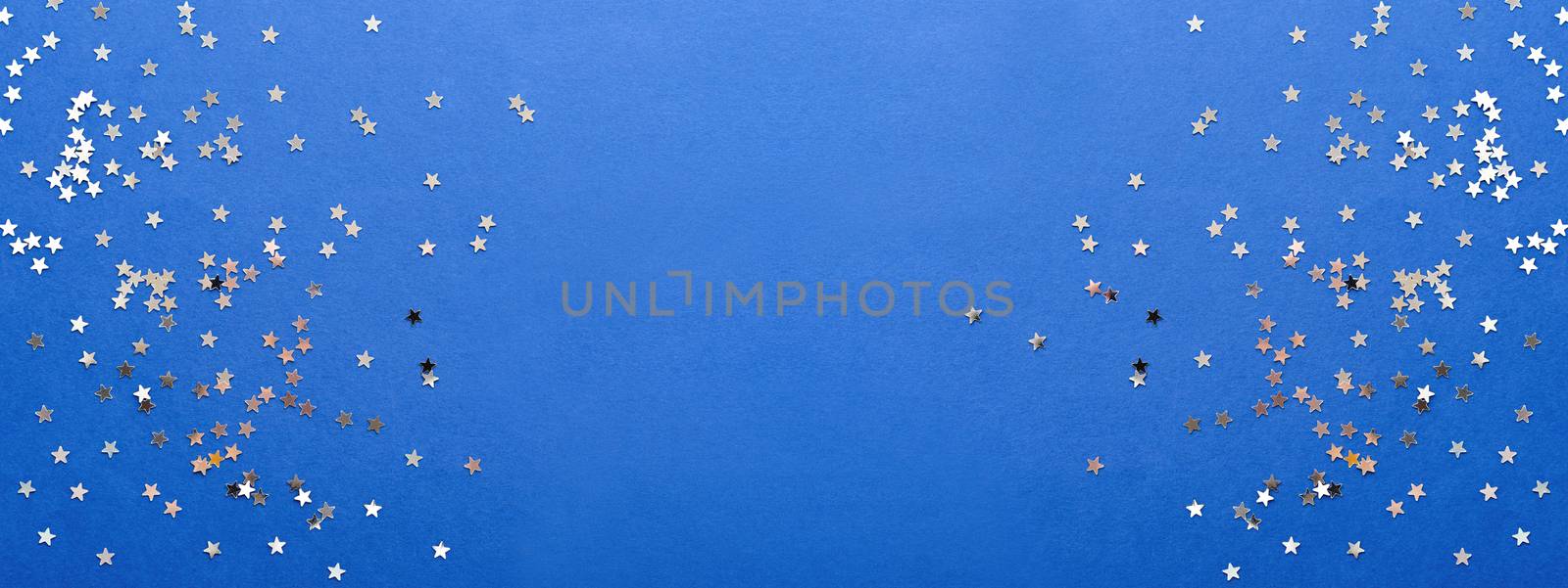 Holiday background with silver star confetti on blue background. Good backdrop for Christmas and New Year cards.
