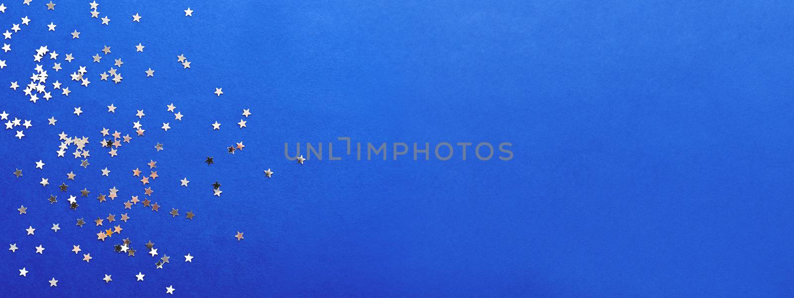 Holiday background with silver star confetti on blue background. Good backdrop for Christmas and New Year cards.