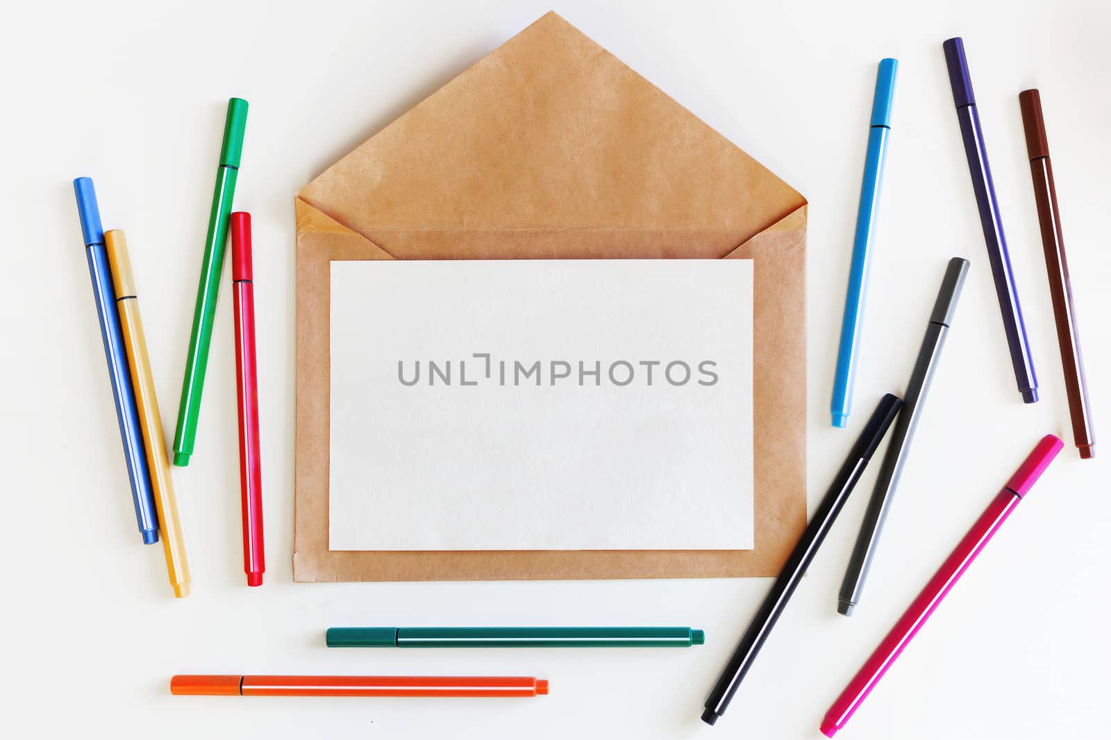 Clear sheet of paper on craft envelope. Background with colorful pens. Mock up. Flat lay, top view.