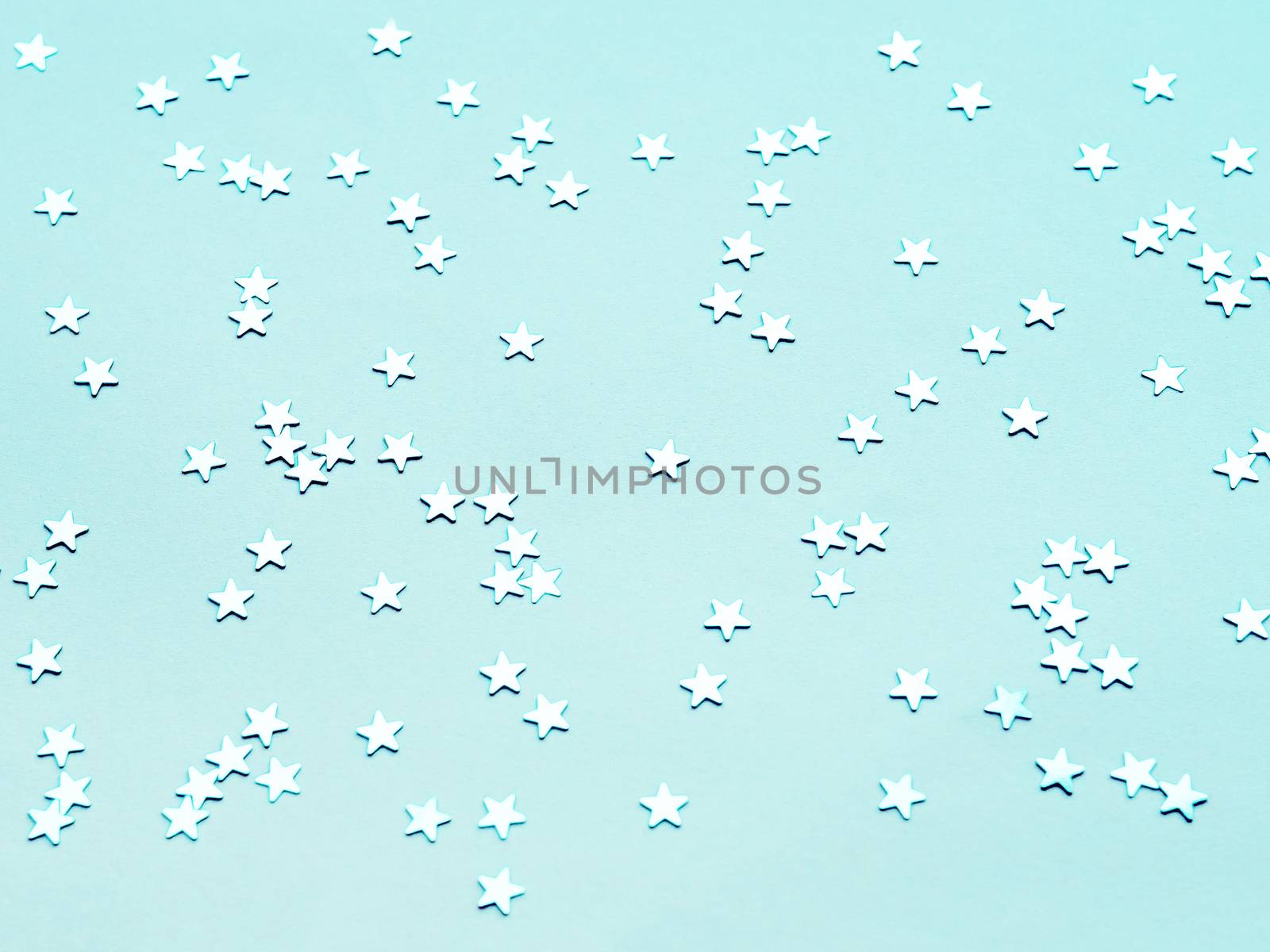 Holiday background with silver star confetti on aquamarine background. Flat lay, top view.