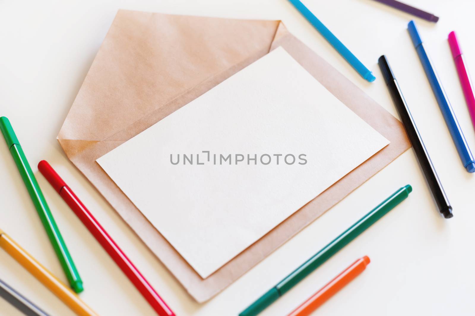Blank sheet of paper on craft envelope. Background with colorful pens. May be used as mock up.