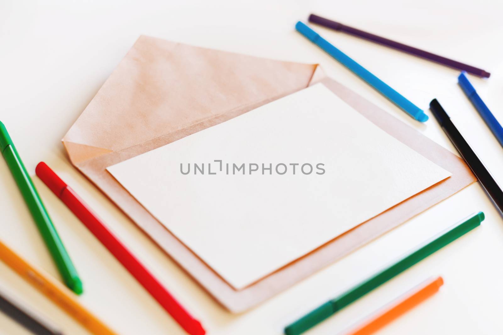 Blank sheet of paper on craft envelope. Background with colorful pens. May be used as mock up.
