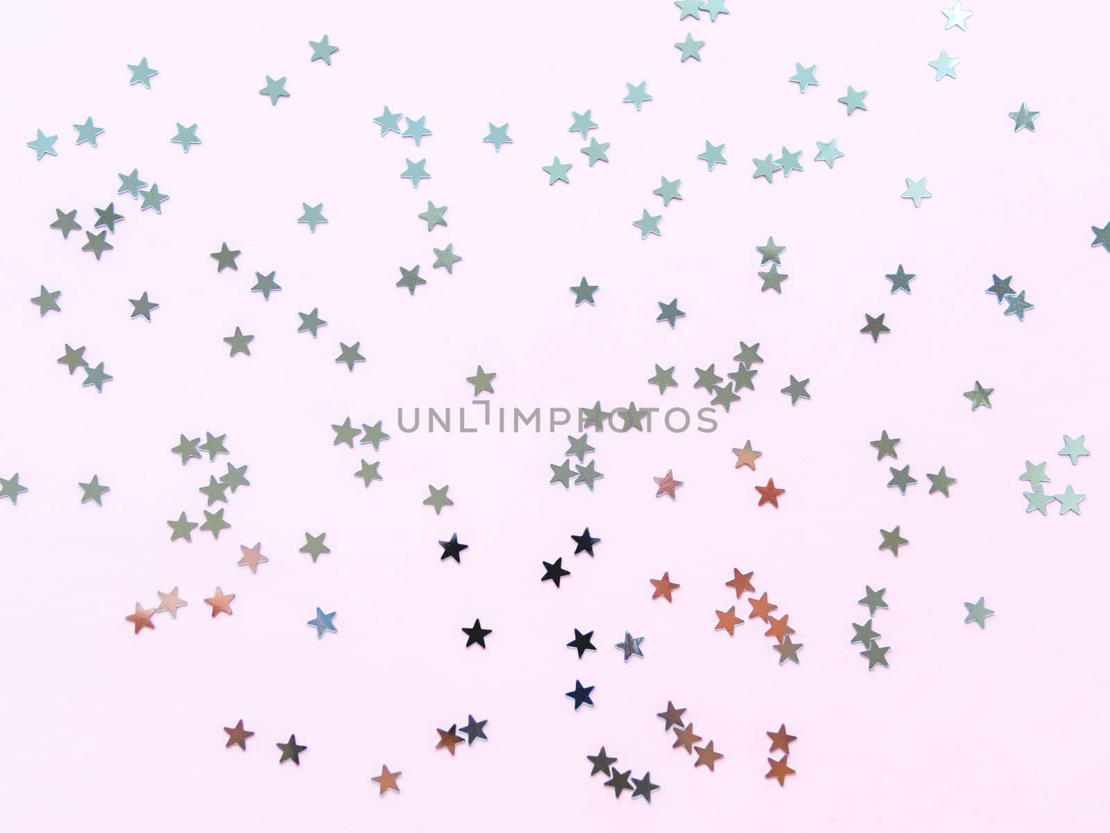 Holiday background with silver star confetti on pink background. Good backdrop for Christmas and New Year cards. Flat lay, top view.